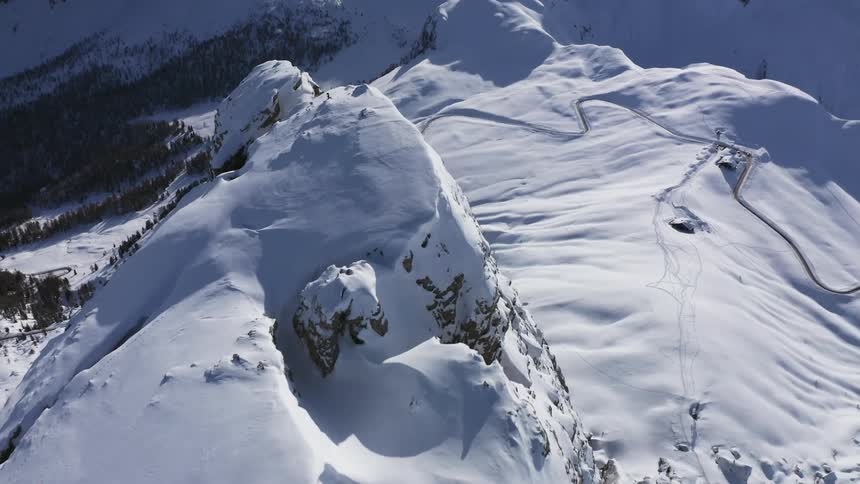 Aerial view of snowy high mountain peak looking over valley with forest