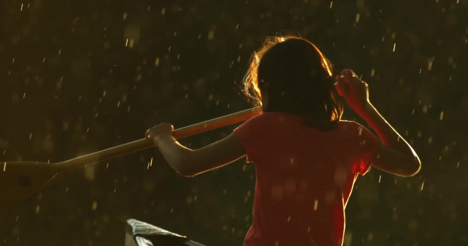 A woman alone in a boat starts to paddle away as rain falls down