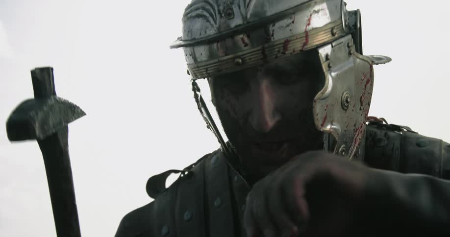 A man in a medieval costume and metal helmet strikes down with his hammer