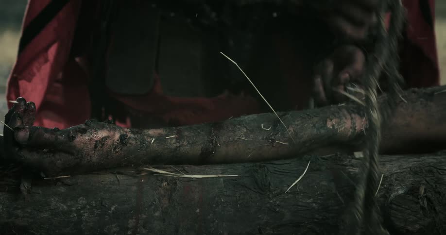 A man in a cape is wrapping a vine around some logs