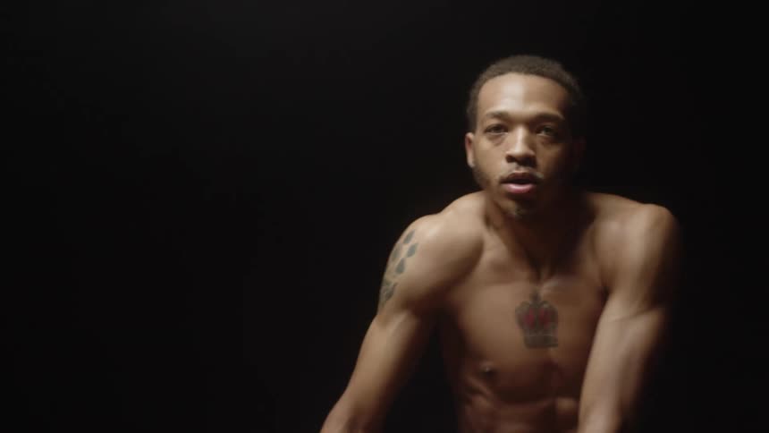 Bare chested male dancer with tattoos dances in dark room under stage lights