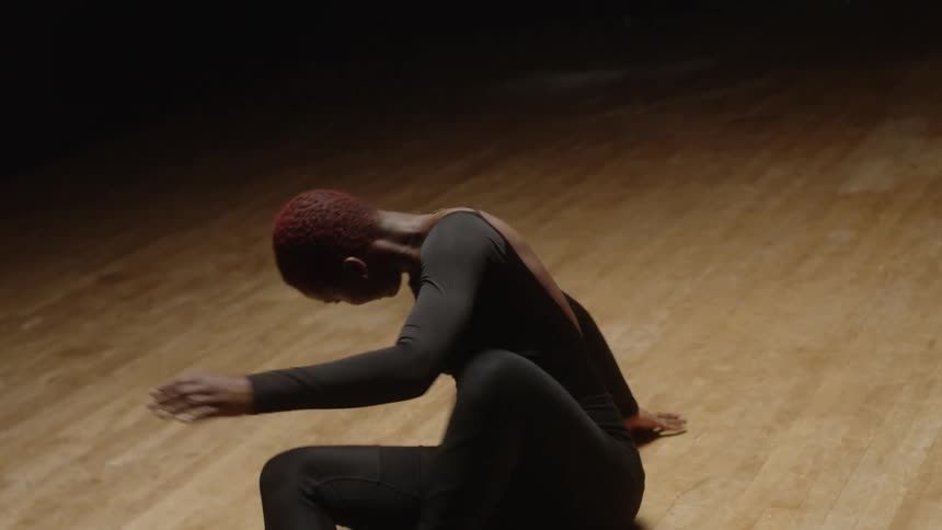 Female dance wearing black dances on wooden floor in dark studio in lighted area