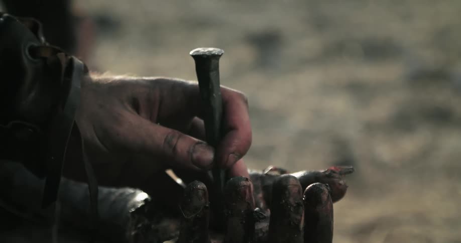 A man places a spike on a hand and gets ready to strike it