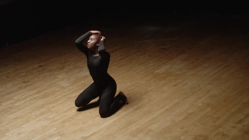 A woman slowly kneels and moves around dancing