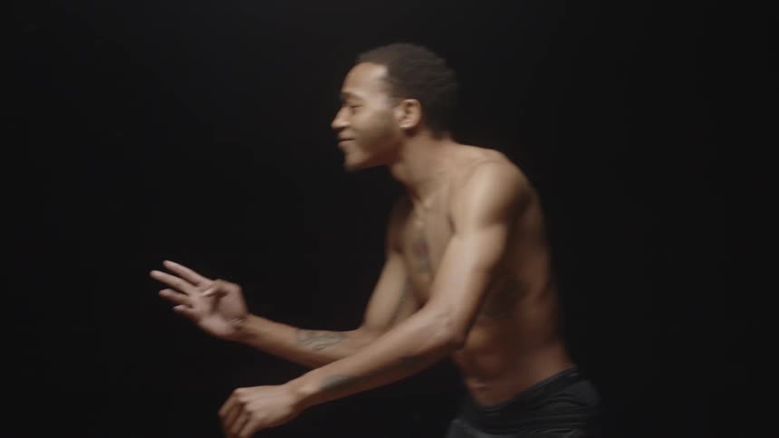 Young muscular shirtless man performing interpretative dance inside a dark room