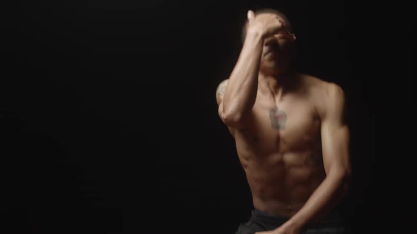 Bare chested male dancer with tattoos performs in dark studio in area lit by light