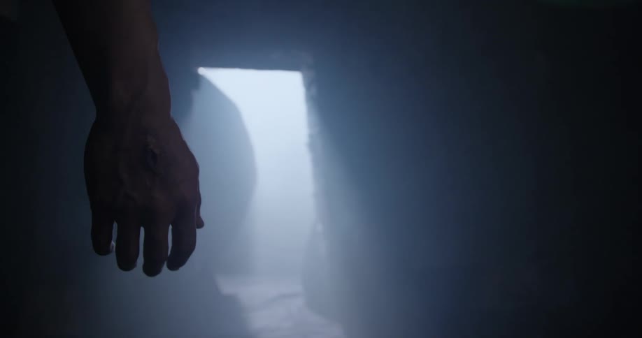 Boulder is rolled from entrance to cave revealing mans hand with nail hole