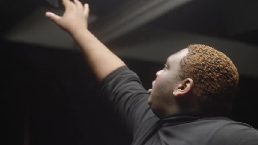 Young man wearing a black sweater performing interpretative dance inside a dark room