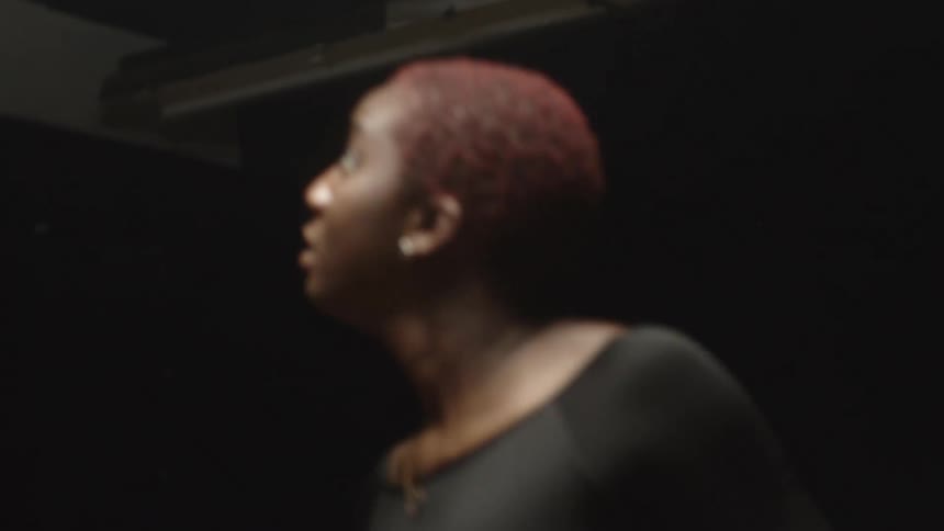 Woman wearing a tight black dress performing modern dance on a dark stage