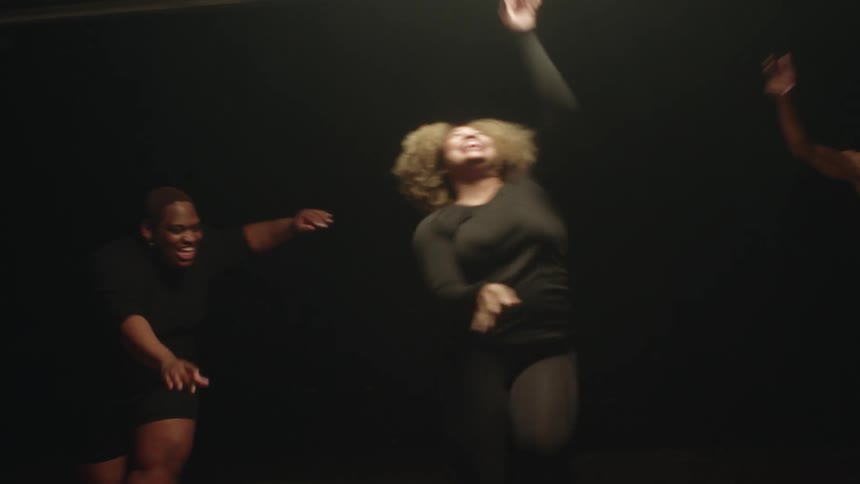 Group of woman wearing thight black dresses happily dancing on a dar stage