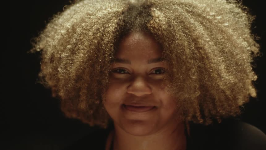 A woman laughs as she runs her hand through her blonde afro