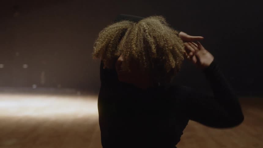 Female dancer performs on dark stage lit by roving spotlight