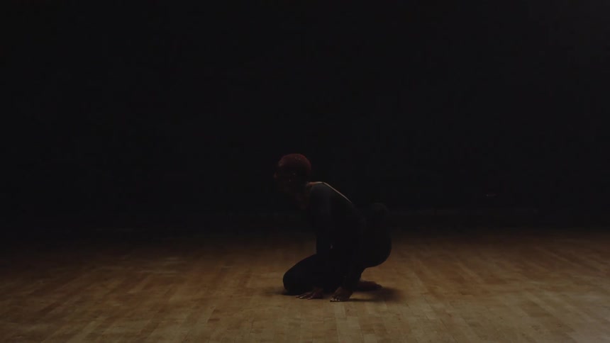 Female dancer wearing leotard moves through dance poses sitting on wooden stage lit by moving stage light