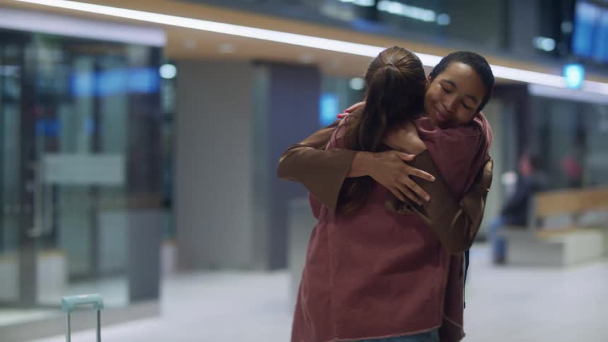 Friends greet each other at airport terminal as others sit and move around terminal