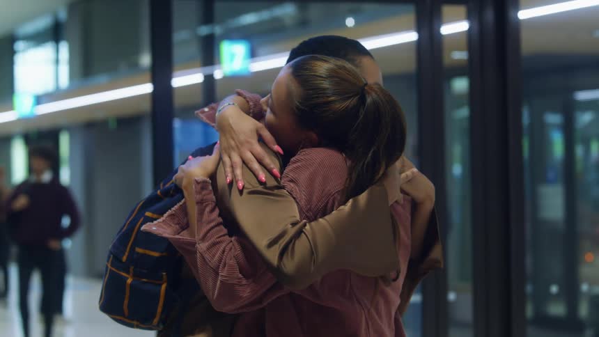 A woman carrying luggage walks up to another woman and gives her a big hug