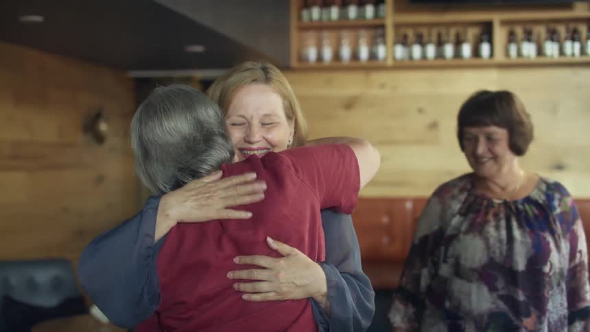 Three women hug and greet in the bar