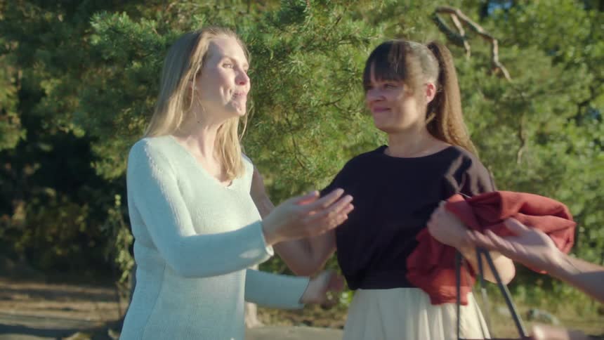 A woman hugs another woman and a man as they talk to each other