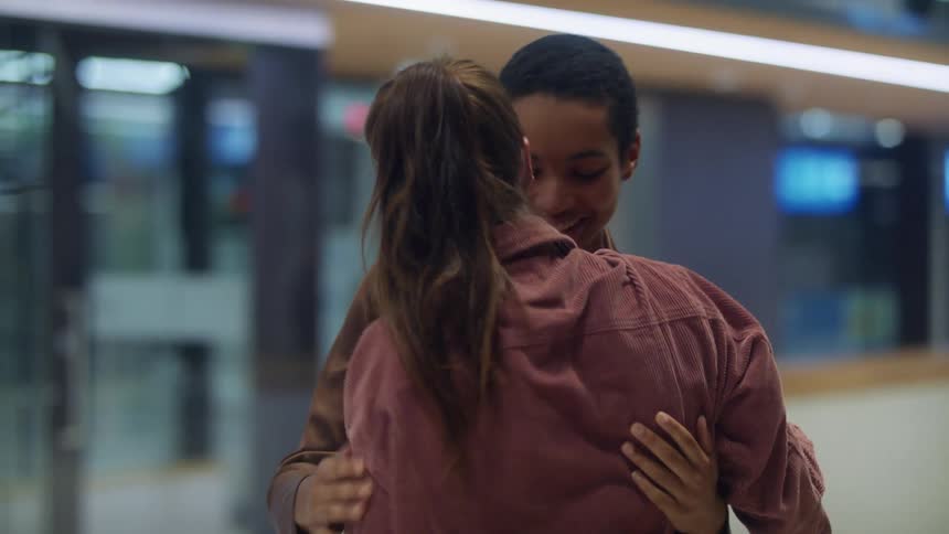 Two young friends greet each other with a hug in a passenger terminal