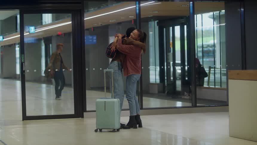 Friends greet each other as one walks out of terminal along with other travelers