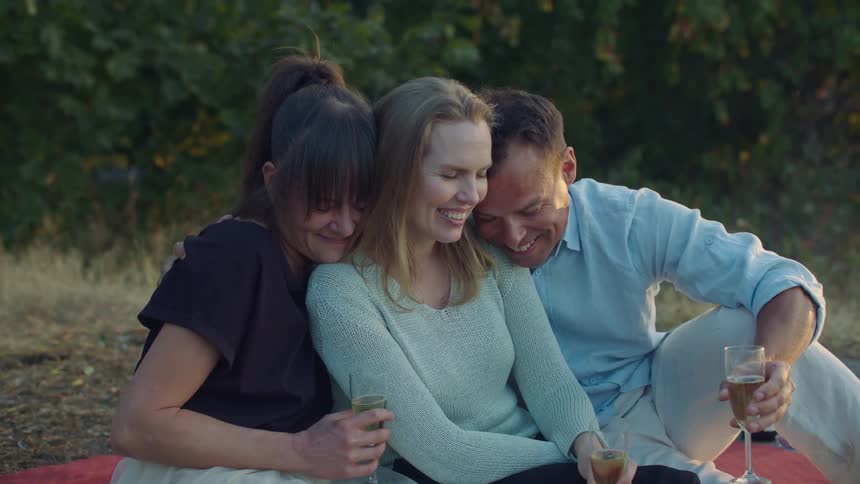 Three people laugh hug and have drinks together