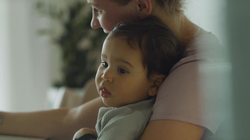 Mother sitting at the table with her son on her arms at home