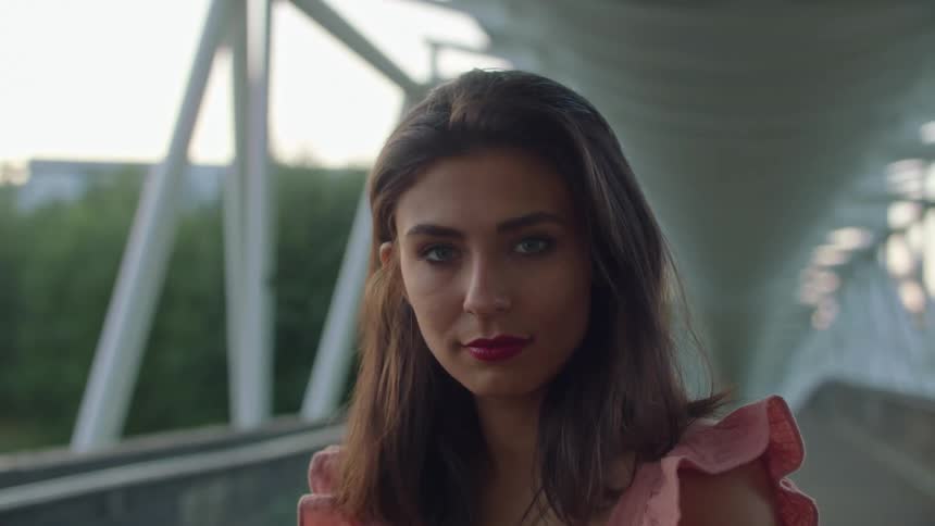 Woman with brown hair and pink blouse faces the camera with eye contact on the bridge