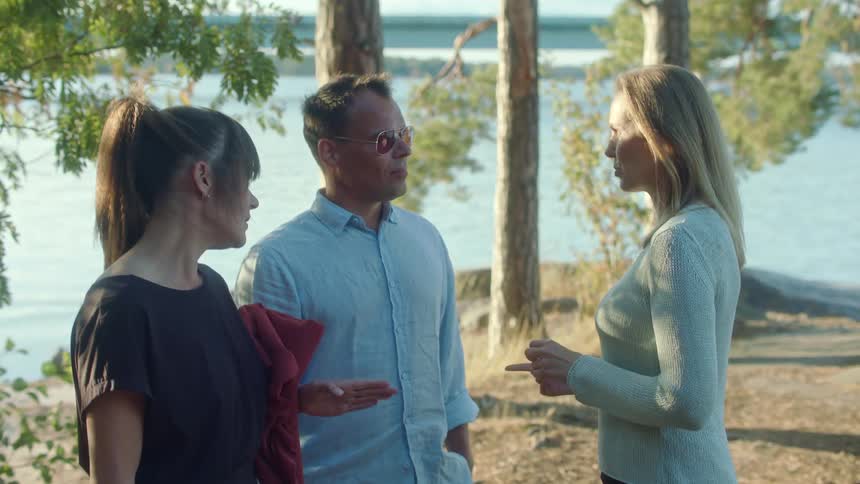 A trio of people stand outdoors while talking and laughing as they socialize