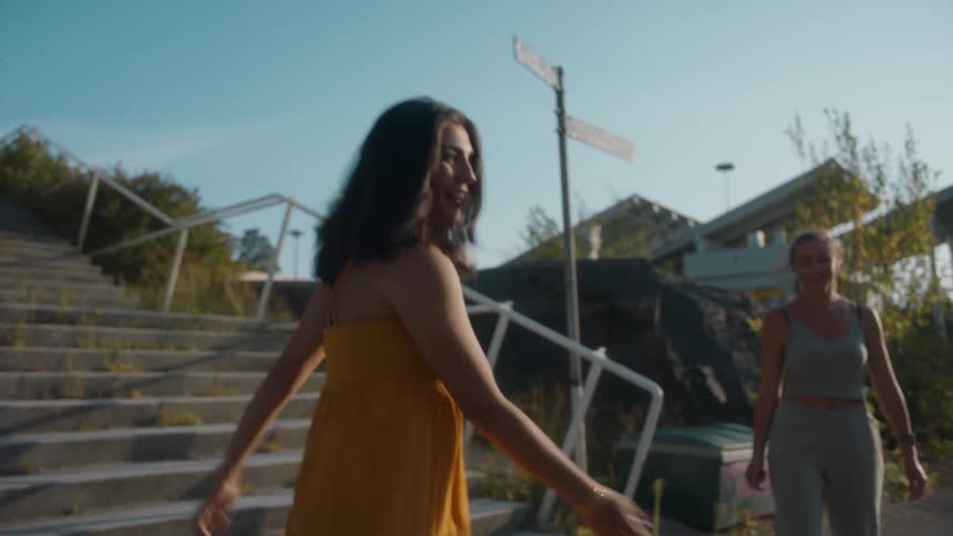 Female friends talk and perform dance steps on sidewalk between concrete stairs and road