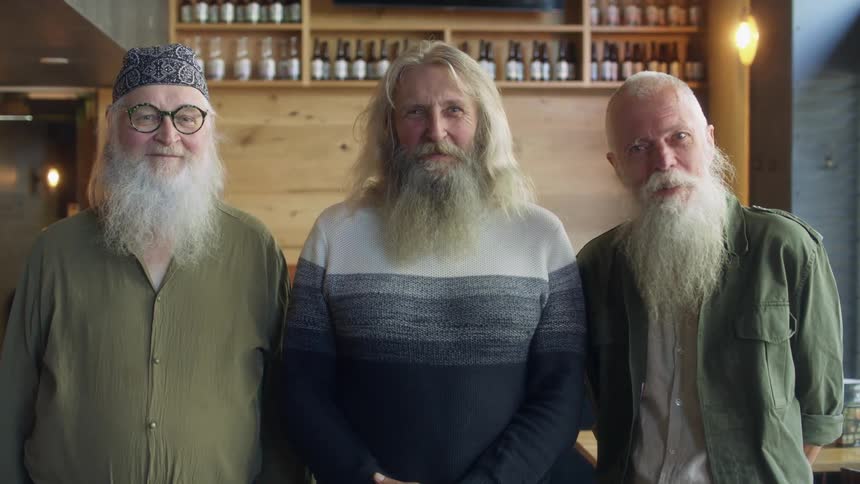 A group of old men with long grey beards and hair looks at camera in pub