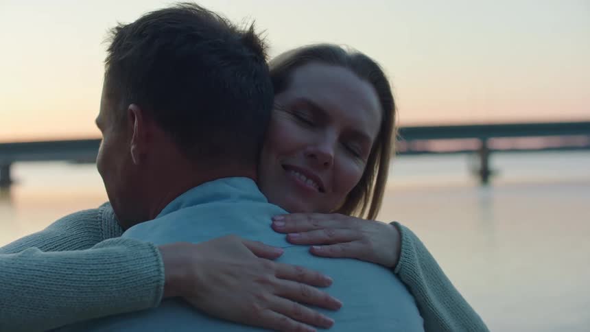 Friends hug and the woman leaves as truck crosses bridge over water behind them