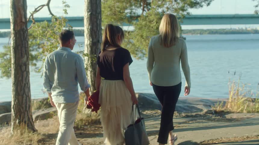 A man and two women walk toward a lake with a blanket