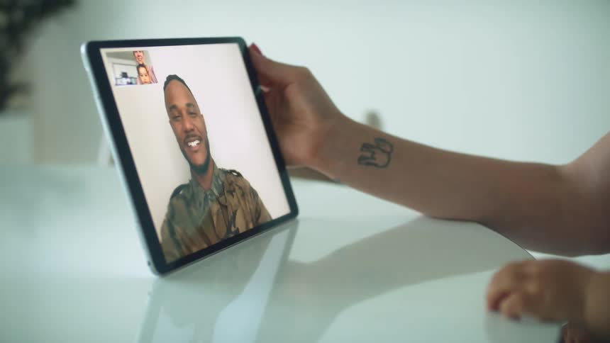 Toddler boy sitting on mothers lap making a video call with man with beard and military uniform on tablet