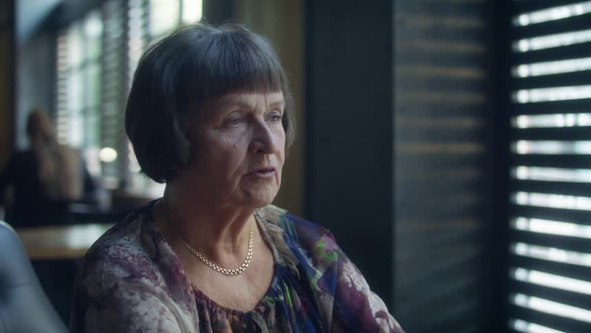 A woman talks while sitting at a table next to a window in a restaurant
