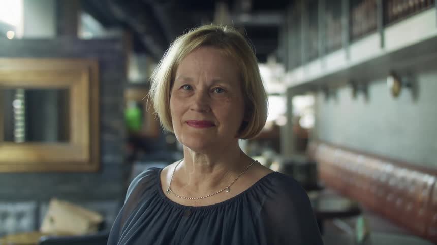 A woman in a room standing and staring with a wall in the background