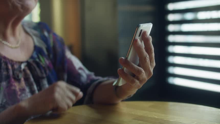 Elderly woman with blue dress sits at table showing picture on smartphone