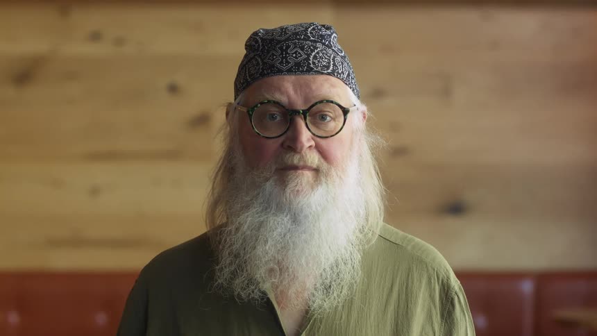 Bearded man wearign glasses standing on a restaurant looking at the camera