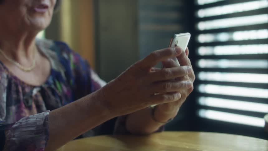 Elderly woman sitting at table shows photographs on smart phone
