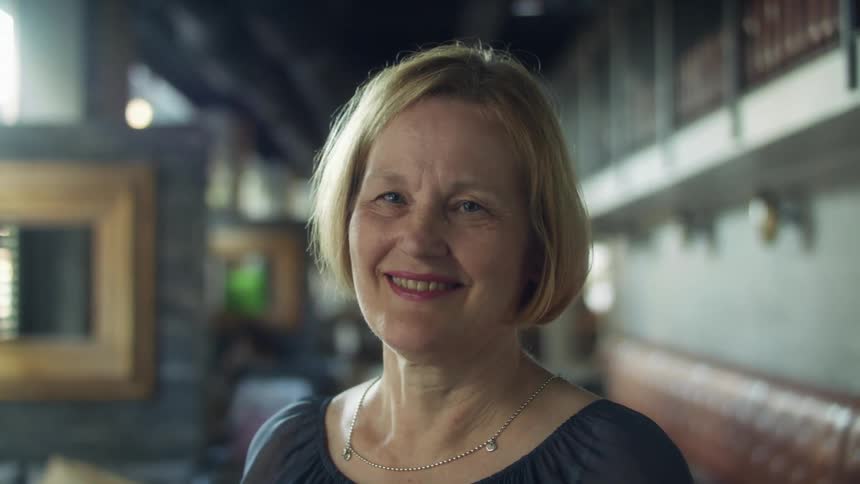 A middle aged woman smiles into the camera while standing indoors during the day