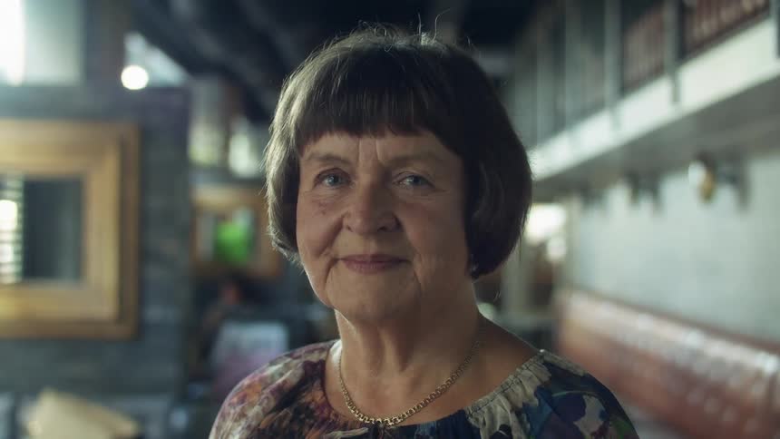 Elderly woman standing on a restaurant looking at the camera