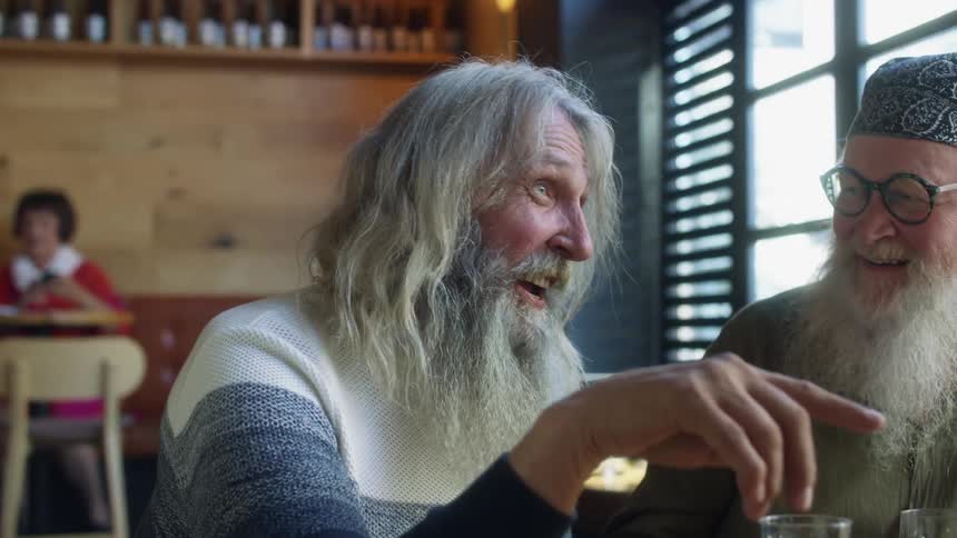 A pair of graying men laugh while chatting at a table in a restuarant