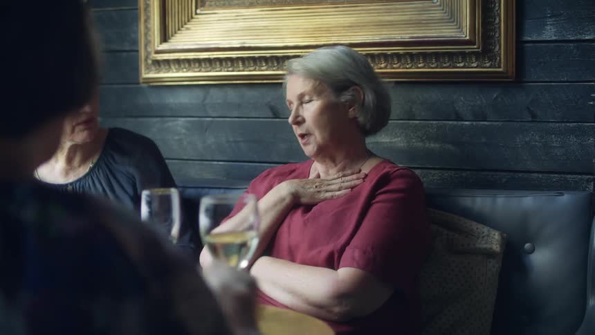 A visibly upset woman is comforted by her friend as they sit at a booth in a pub with wine glasses on the table