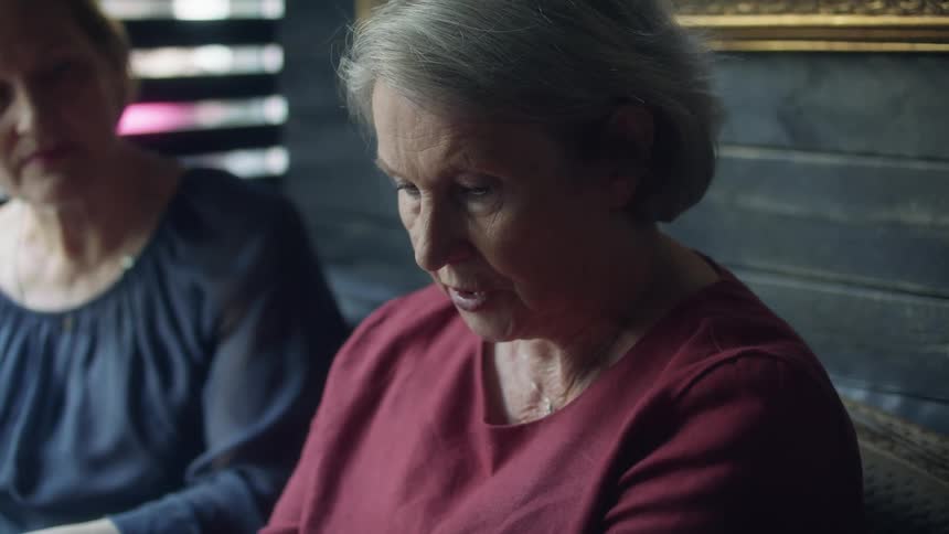 Older woman talks looking downcast and another woman comforts her by patting her