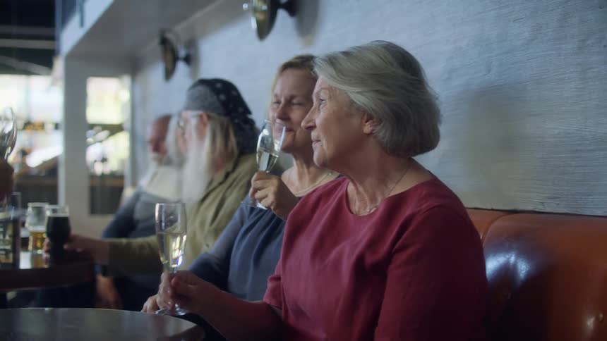 Older friends sit at restaurant drinking wine and talking