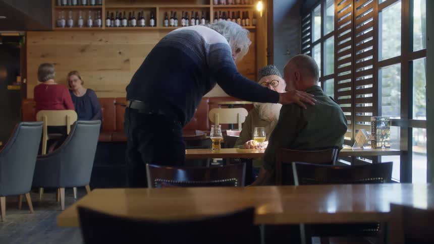 A man gets up from the table to shake his friends hand