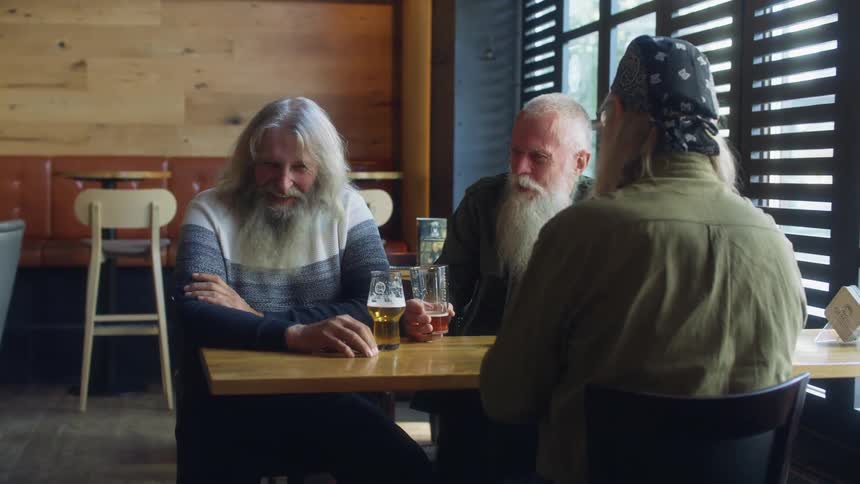 Three men sitting at a table in a bar with a wall and a window in the background