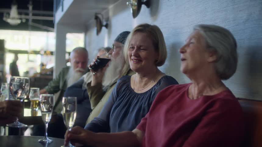 A mature group of family and friends enjoy drinks and happy conversation in a diner during the day
