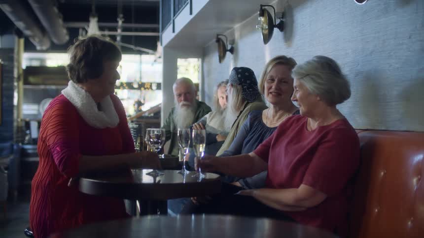 A group of mature adults are sitting in a diner having drinks and conversation during the day