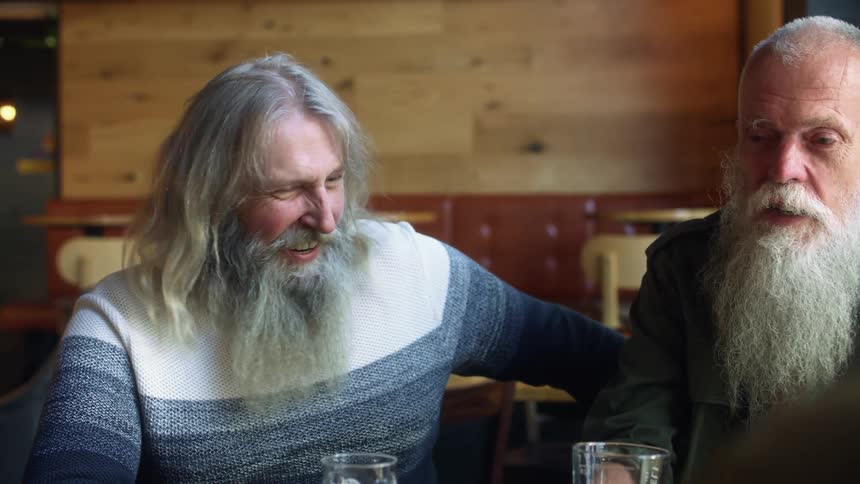 A pair of men sit together while talking and laughing over a few glasses of beer