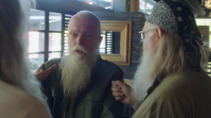 Three elderly ment greet each other by shaking hands in a restaurant