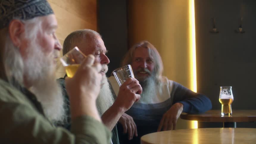 Group of bearded friends talking and drinking beer while laughing in a bar